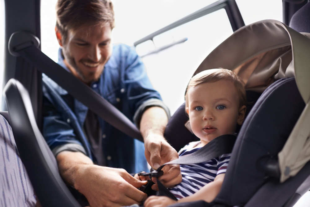 Photo of a dad buckling up his child in a car seat