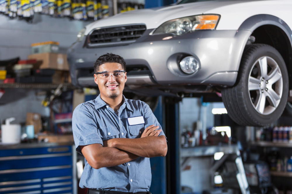 Image of smiling mechanic in front of a car in an auto repair garage