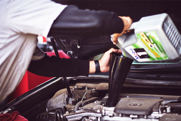 Closeup image of a mechanic pouring motor oil into a car engine