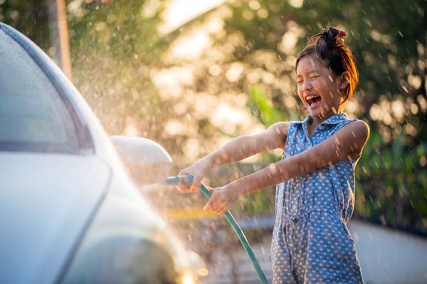 Photo of a girl with a hose in hand washing a car